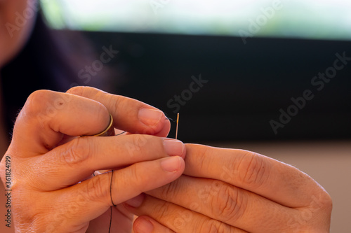 Detail of woman's hands threading a sewing needle at home