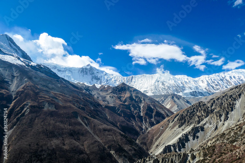 A panoramic view on a valley along Annapurna Circuit in Nepal. In the back there are high, snow capped Himalayan peaks. Slopes are overgrown with small bushes. Exploration and discovering