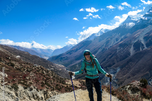 Woman enjoying her trek to Tilicho Lake, along Annapurna Circuit in Nepal. In the back there are high, snow capped Himalayan peaks. Slopes are overgrown with small bushes. Exploration and discovering