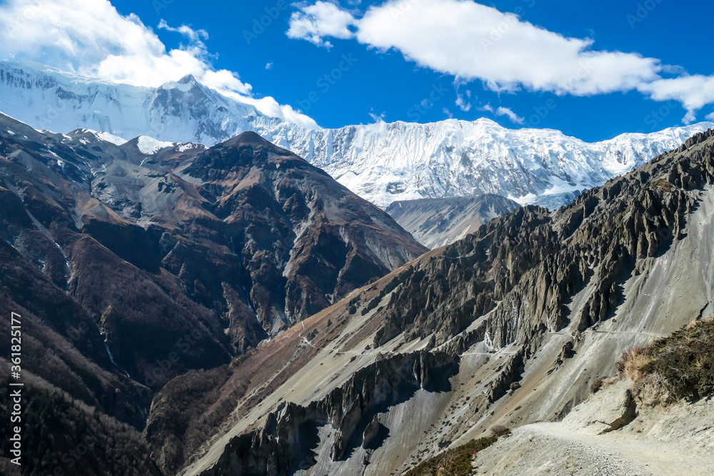 A panoramic view on a valley along Annapurna Circuit in Nepal. In the back there are high, snow capped Himalayan peaks. Slopes are overgrown with small bushes. Exploration and discovering