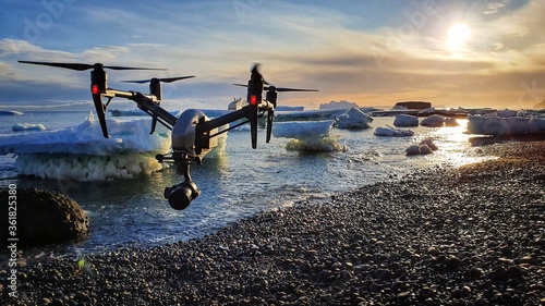 Drone flying under sunrise over a pebble beach with icebergs in the background