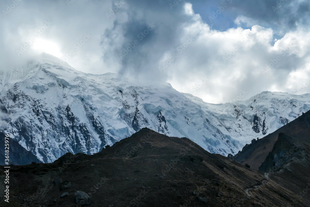 A close up view on high, snow capped Himalayan peaks along Annapurna Circuit in Nepal. Barren and sharp slopes. Mountains are partially shrouded with clouds. Exploration and discovering new places