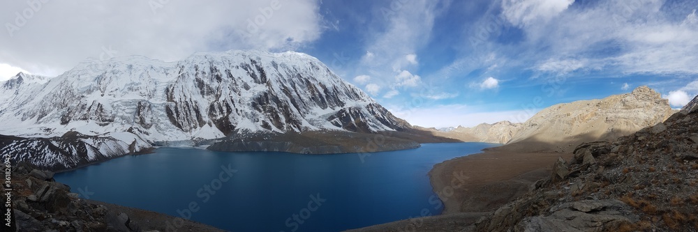 Naklejka premium A panoramic view on turquoise colored Tilicho lake in Himalayas, Manang region in Nepal. The world's highest altitude lake (4949m). Snow capped mountains around. Calm surface of the lake. Serenity