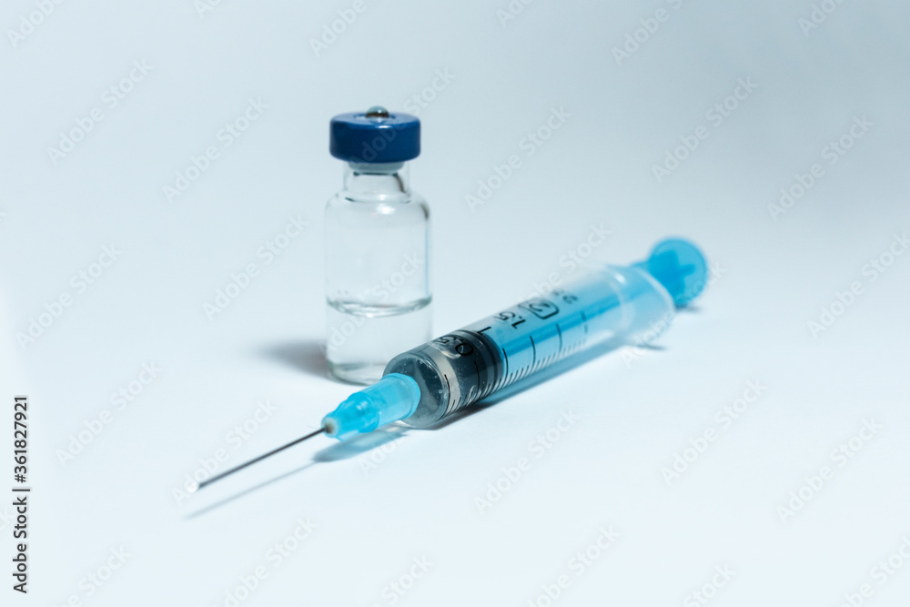 Glass medicine bottle with injection fluid with blue aluminium cap and syringe for vaccination. Cancer, painand diabetes treatment, pharmaceutical medicine concept . Glass medicine bottle with injection fluid with blue aluminium cap and syringe for vaccination. Cancer, painand diabetes treatment, pharmaceutical medicine concept .