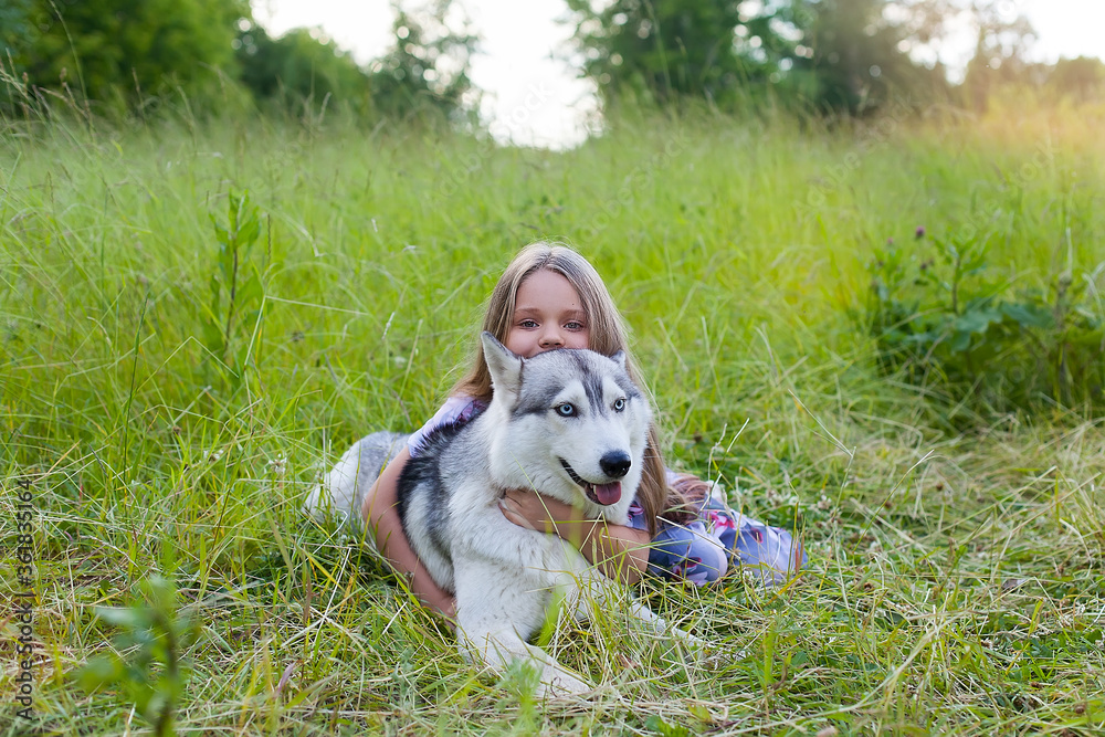 the girl and her dog were lying on the grass together. A happy child hugs his pet husky, smiles.