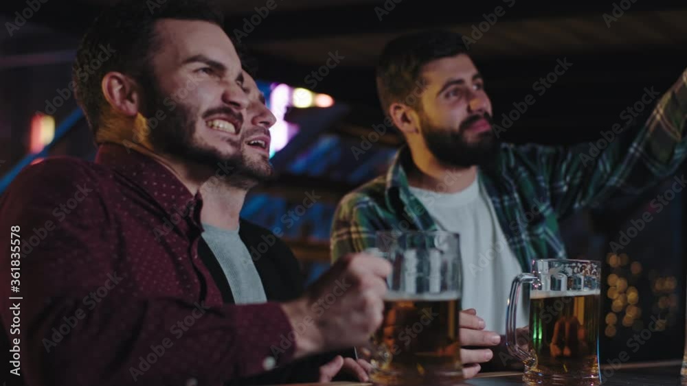Closeup to the camera charismatic good looking guys in a pub watching a fav match on tv while drinking beer they are very concentrated and excited