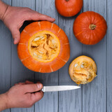 Men's hands with a knife cut a pumpkin on a gray wooden table. Halloween concept.