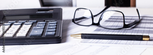 Glasses, a calculator and pen lie on the reports. Close up business concept