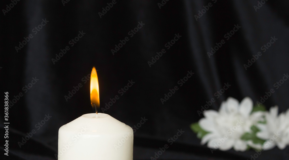 Condolence card. White memorial candle with white flowers in the background. Black background. Condolence card. White memorial candle with white flowers in the background. Black background.