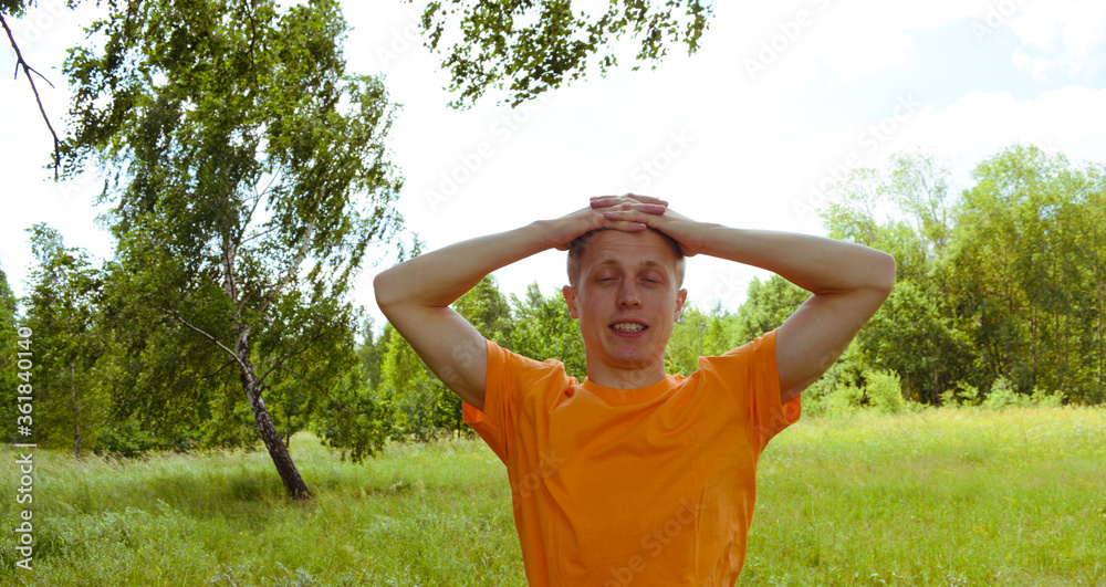 Young man holding his head in an orange T-shirt on nature in the grass Young man holding his head in an orange T-shirt on nature in the grass