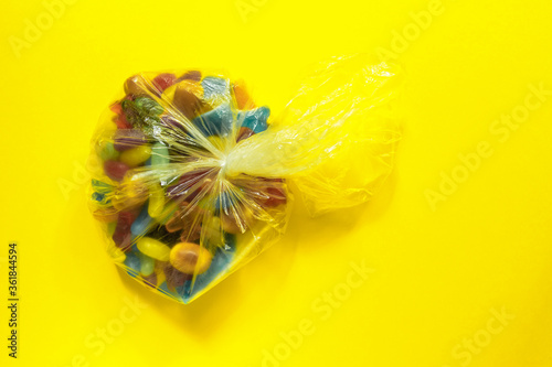 Multi-colored glazed jelly beans sweets in plastic package on yellow paper background
