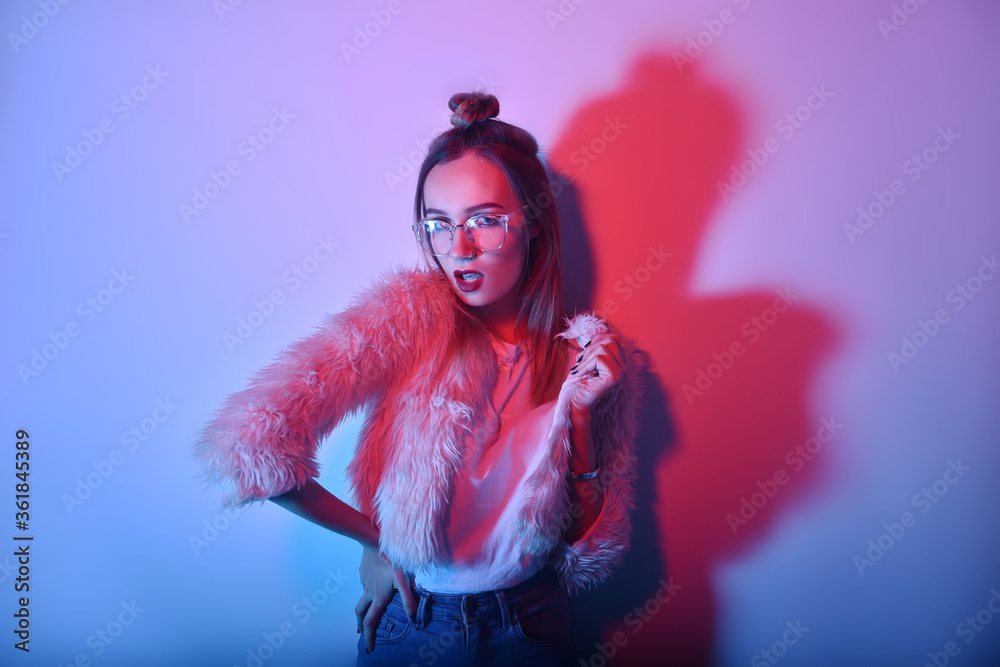 A girl in neon is dancing against a red-blue background. Hipster girl with fashionable haircut and glasses dancing, posing. Model in a fur coat at the club. A girl in neon is dancing against a red-blue background. Hipster girl with fashionable haircut and glasses dancing, posing. Model in a fur coat at the club.