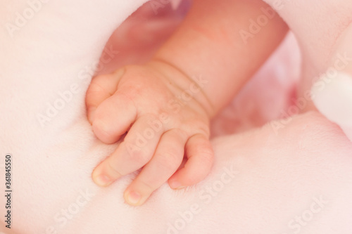 Mão de bebê em close up segurando uma mantinha rosa fofa. Detalhes do braço de um recém nascido com um paninho.