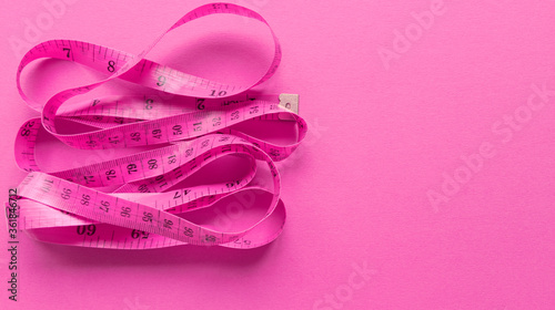 Pink centimeter on pink background. Simple flat lay with pastel texture. Fitness concept. Stock photo.