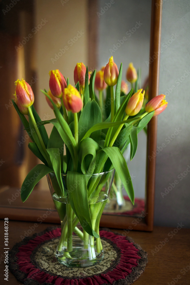 Bouquet of red-yellow tulips in glass vase in front of a mirror, home decor, still life, selective focus