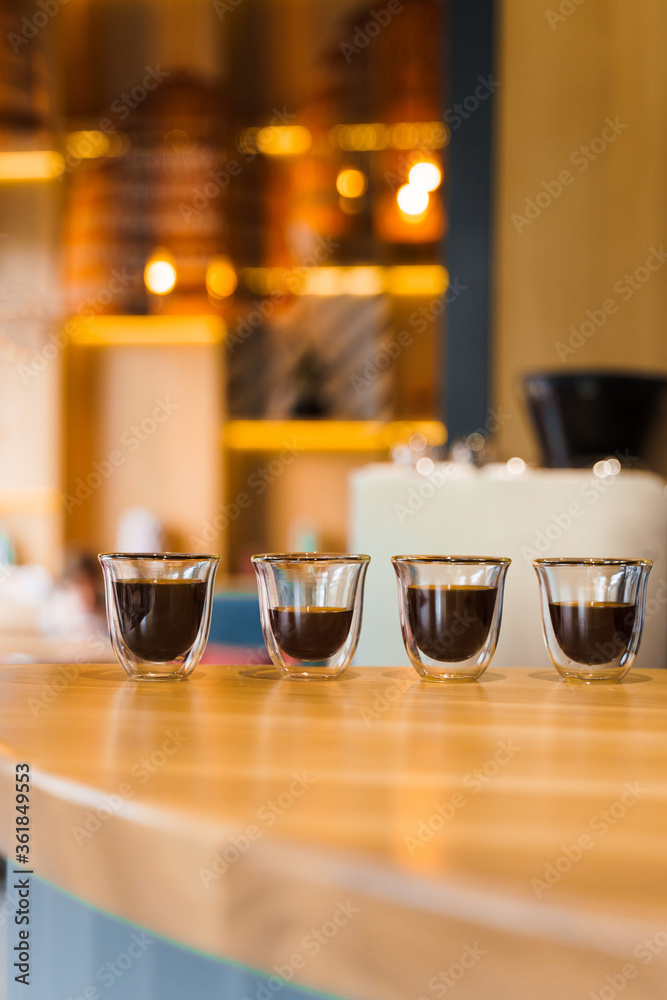 4 Flavored coffee espresso in double glass cup with sun light on background in cafe. Coffee on the wooden table with blurred background. Vertical photo for advert in social networks.