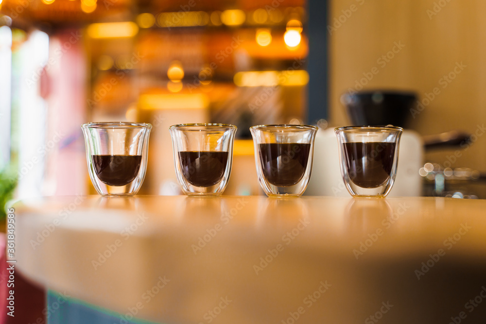 4 Flavored coffee espresso in double glass cup with sun light on background in cafe. Coffee on the wooden table with blurred background