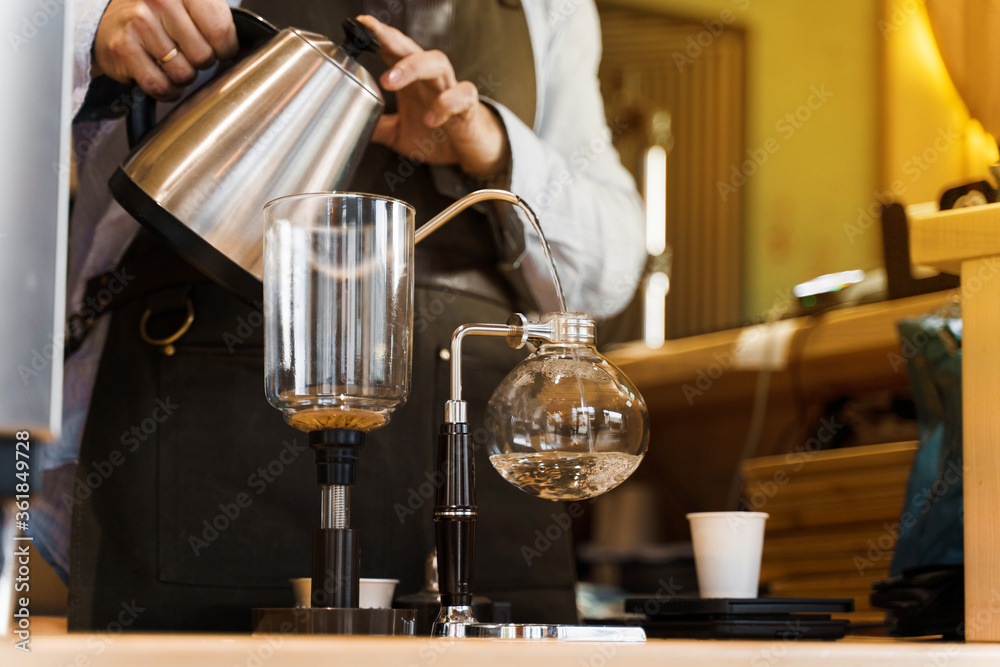 Syphon alternative method of making coffee. Barista pours hot boiling water in syphon device for coffee brewing in cafe. Scandinavian method of coffee making.