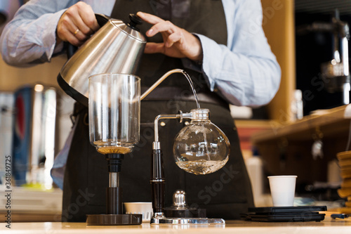 Syphon alternative method of making coffee. Barista pours hot boiling water in syphon device for coffee brewing in cafe. Scandinavian method of coffee making.