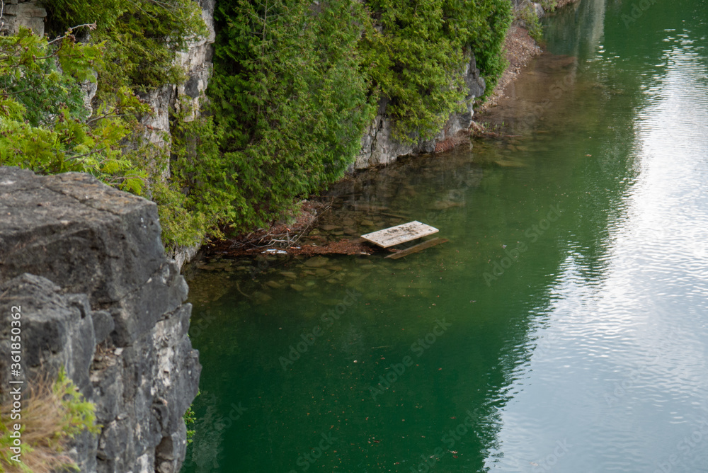 sunken dock in flooded green water surrounded by trees and cliff