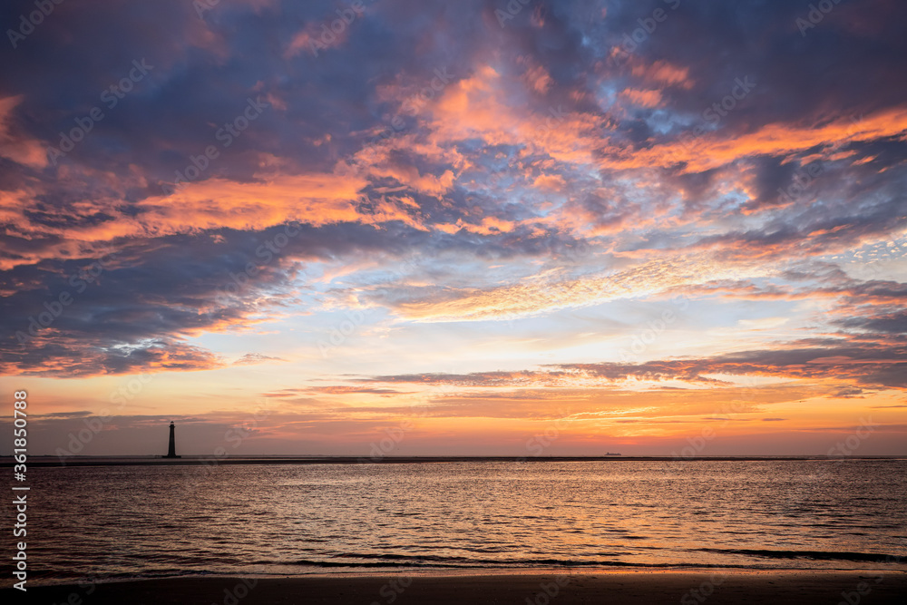 Naklejka premium Photographed from Folly Island, the historic Morris Island Lighthouse and a ship on the horizon are silhouetted by a colorful sunrise sky over the Atlantic Ocean near Charleston, South Carolina.