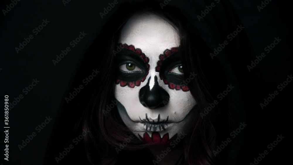 Girl with the traditional day of the dead makeup smiles and shows a grin. Theme of costumes and transformation for holiday of Halloween. Standard skull makeup for feast of Santa Muerte celebration