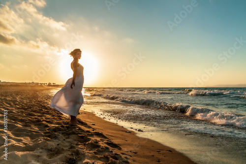 Backlit woman feeling free and happy, breathing clean fresh ocean air on a sandy beach in summer at dusk. photo