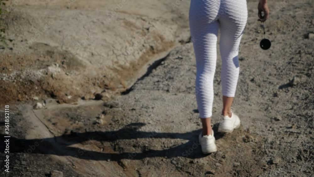 Women's buttocks in white leggings close-up. The buttocks of a sports girl walking along the sandy shore with a shaker in her hands. Women's buttocks in white leggings close-up. The buttocks of a sports girl walking along the sandy shore with a shaker in her hands.