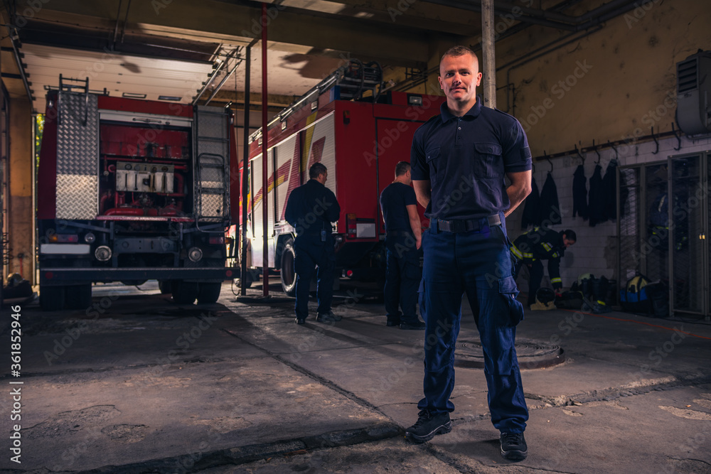 Portrait of handsome firefighter standing against trucks at fire station