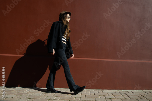 A stylishly dressed girl poses against a red wall. Street fashion