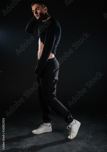 Sexy male model lifting his black blouse and showing his abs while posing in a studio on a black backgorund.