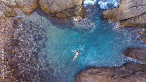 Photography Aerial view of young woman in the blue sea among rocks, oaxaca mexico from above