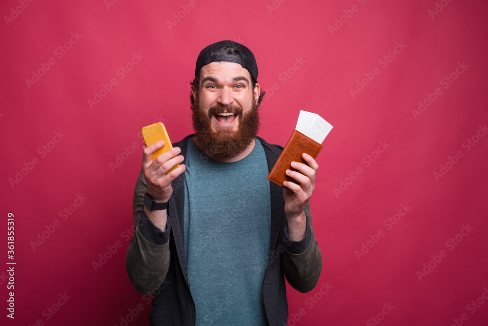 Portrait of a surprised man holding his passport with tickets and his phone Portrait of a surprised man holding his passport with tickets and his phone