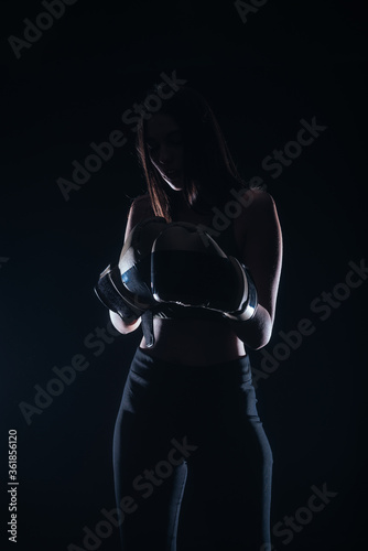 Silhouette portrait of a sexy fit woman posing in dark contrast with boxing gloves