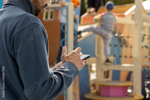 Photography Dad looks at his phone and does not follow children in the playground