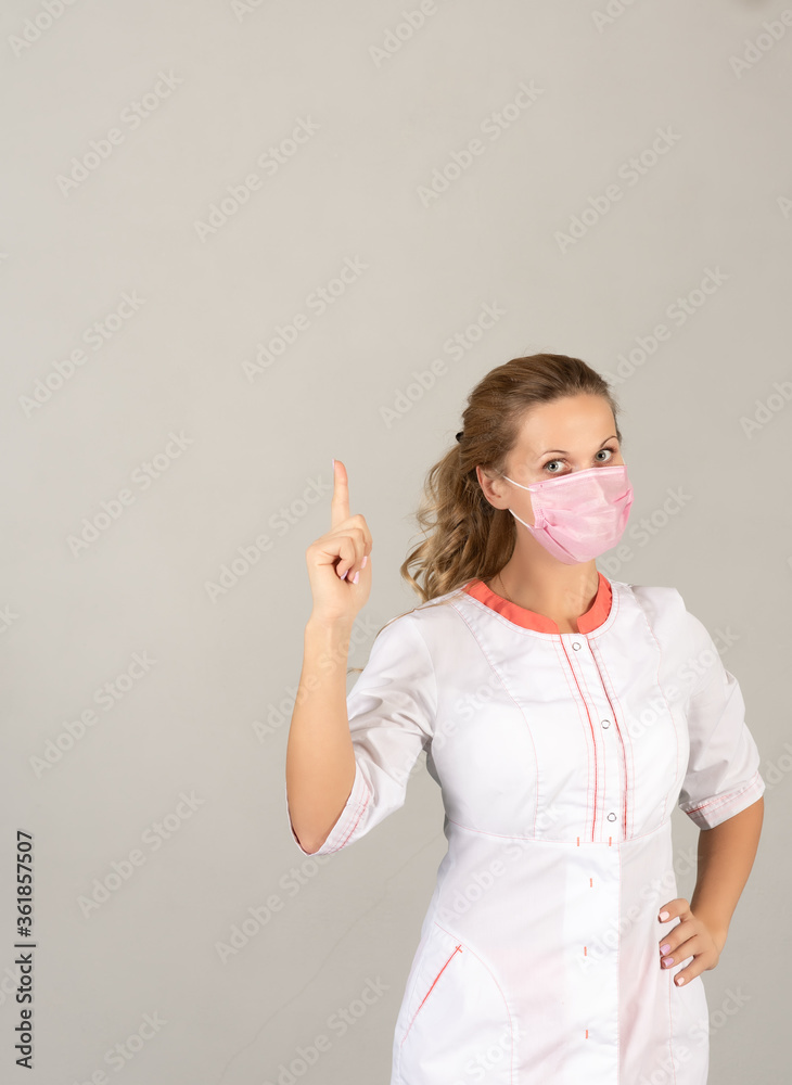 A woman in a protective medical mask and white coat points to a place for text.
