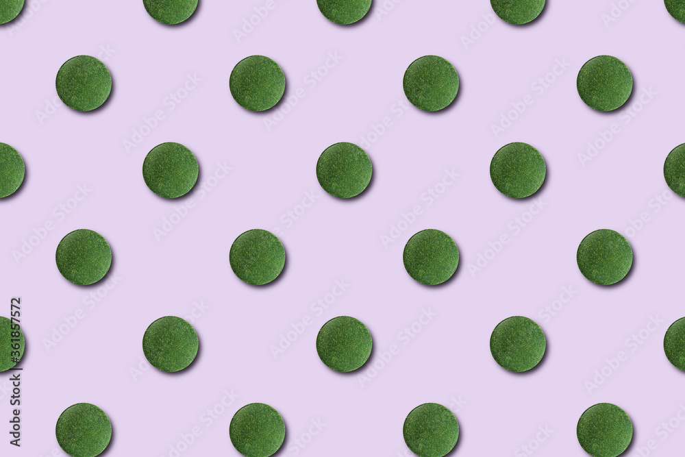 Seamless pattern of green chlorella or spirulina tablets on a pink background.