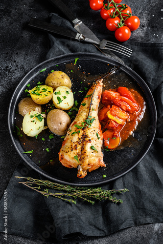Baked in tomatoes monkfish with potatoes and vegetables. Black background. Top view