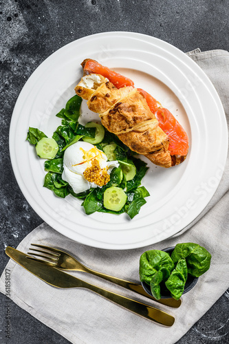Croissant with salmon and ricotta cheese, side salad with spinach and egg. Back background. Top view