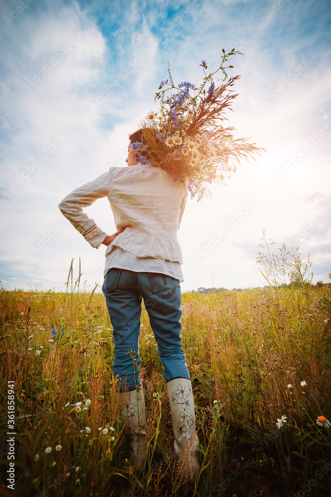 Fototapeta premium beautiful young girl in a field of flowers enjoys the aroma and view of field daisies.