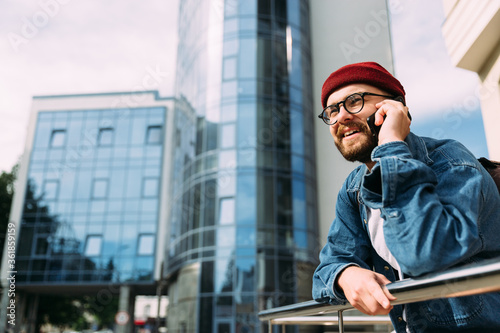 Cheerful handsome young bearded hipster male talking on phone and smiling