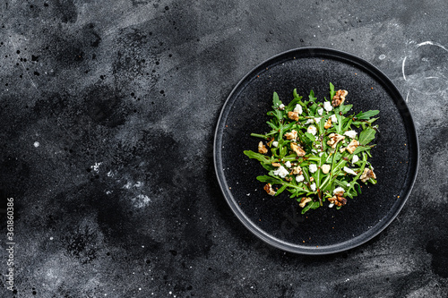 Healthy salad with arugula, goat cheese, nuts and vinaigrette sauce. Black background. Top view. Copy space