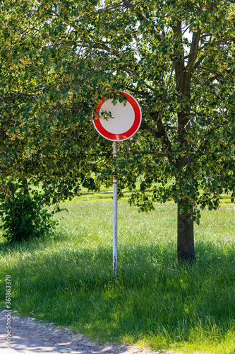 Road sign prohibiting the entry of motor vehicles, which is hidden behind tree branches.