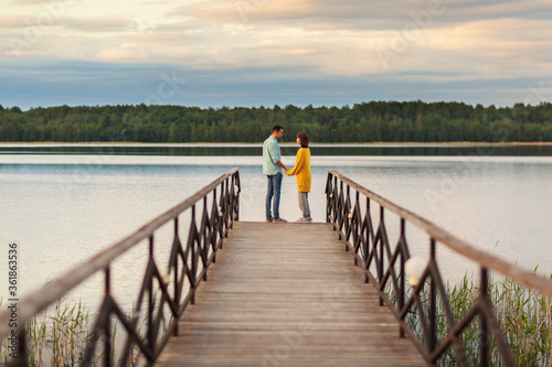 Romantic young couple standing face to face on wooden pier over river and talking. Man declaring his love to girlfriend