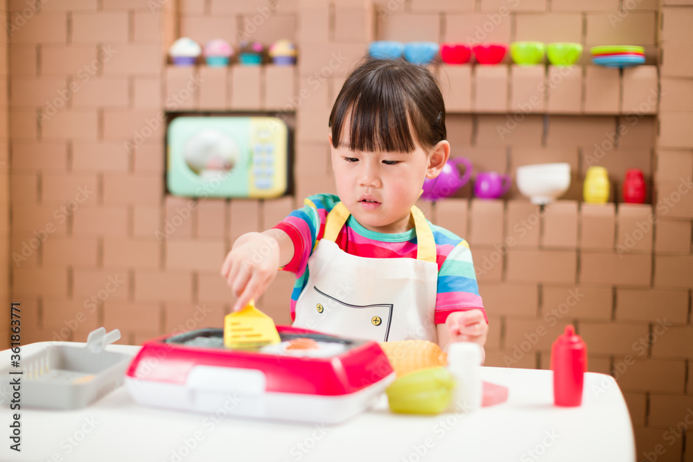 toddler girl pretend play food preparing role against cardboard blocks kitchen background toddler girl pretend play food preparing role against cardboard blocks kitchen background