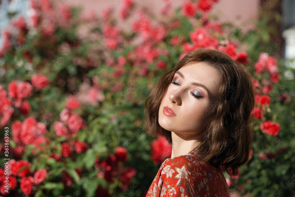 Young beautiful dreamy woman with closed eyes posing in the rose garden. Outdoor fashion portrait of romantic girl with hard light. Young beautiful dreamy woman with closed eyes posing in the rose garden. Outdoor fashion portrait of romantic girl with hard light.