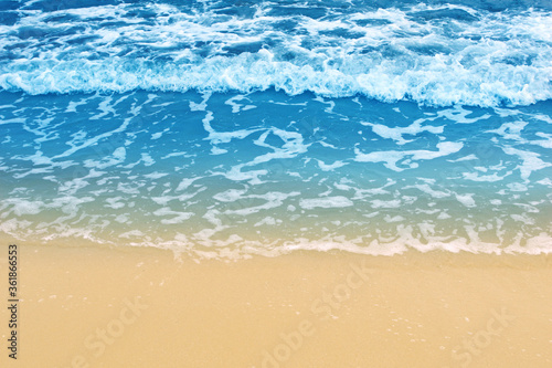 Soft wave of blue ocean on sandy beach. Background. Empty beach with sea foam washing up from sea.