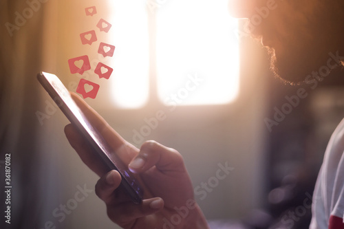 man holding smart phone in house with heart icons hovering over the screen social media concept