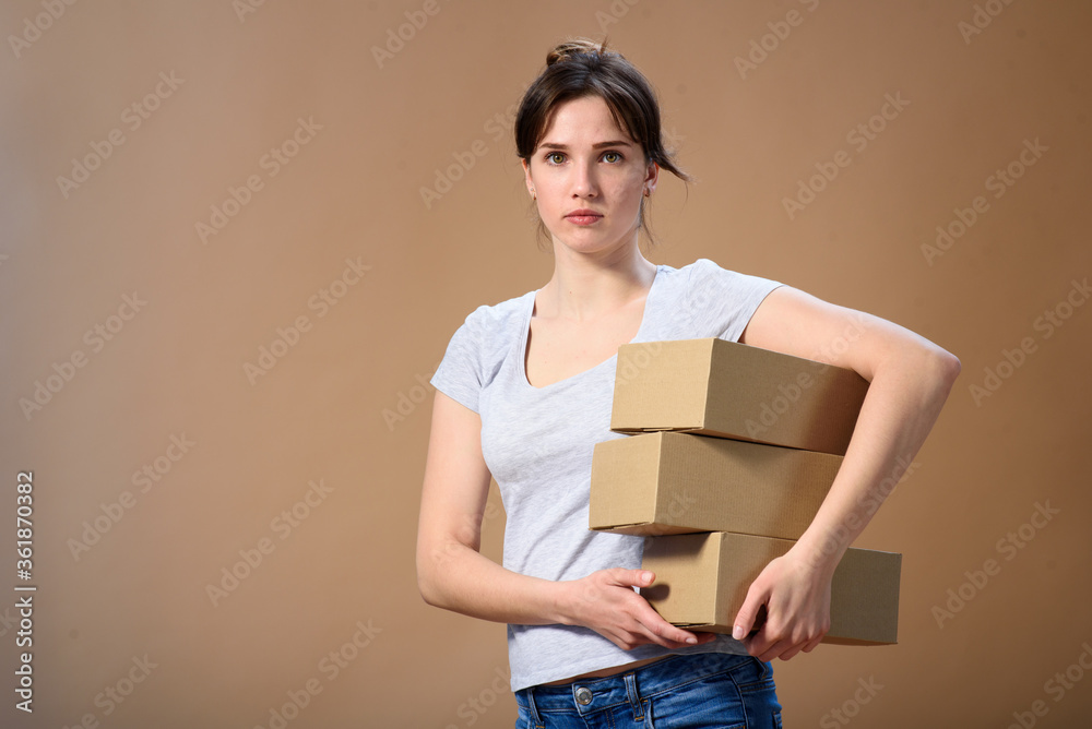European girl holds several boxes in her hands with her side and looks at the camera directly on a beige wall European girl holds several boxes in her hands with her side and looks at the camera directly on a beige wall