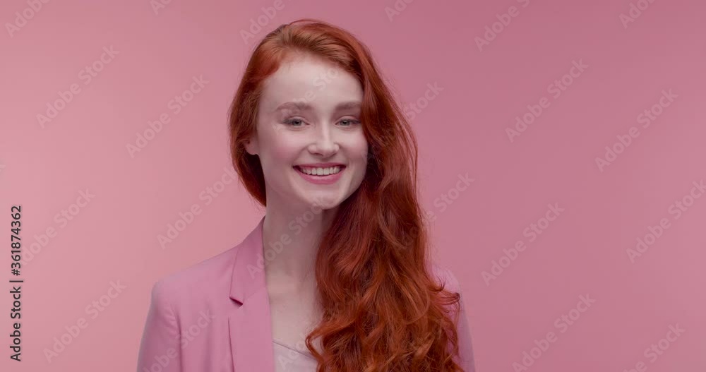 Beautiful female Model posing on Camera, standing in the Foreground, enjoying her Job. Looking Pretty and Stylish, wearing trendy Pink Jacket. Pink wall in the Background. Charming red hairstyle. Beautiful female Model posing on Camera, standing in the Foreground, enjoying her Job. Looking Pretty and Stylish, wearing trendy Pink Jacket. Pink wall in the Background. Charming red hairstyle.